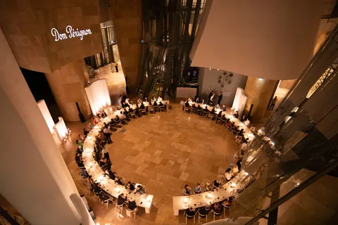 Dom Pérignon Révélations 2026: runde Dinnertafel von oben, Gäste im Kerzenlicht unter dem Schriftzug Dom Pérignon